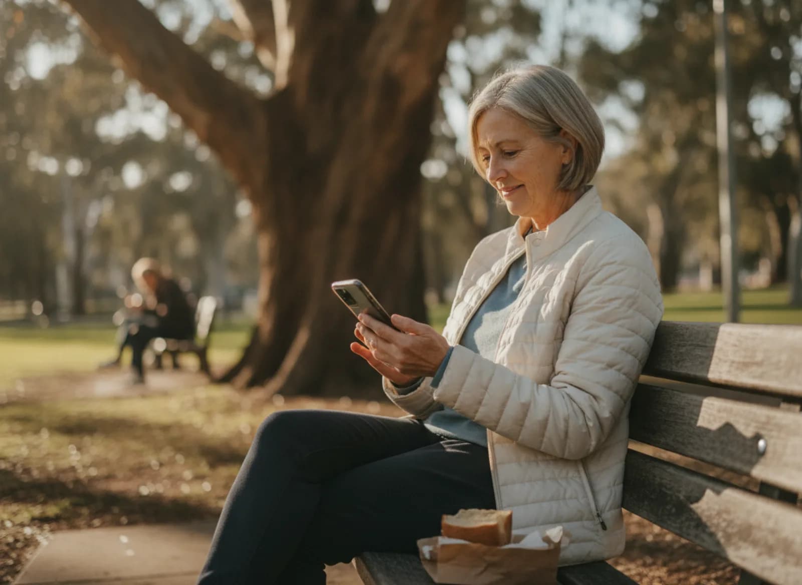 A woman on a park bench at lunch reading a message on her phone
