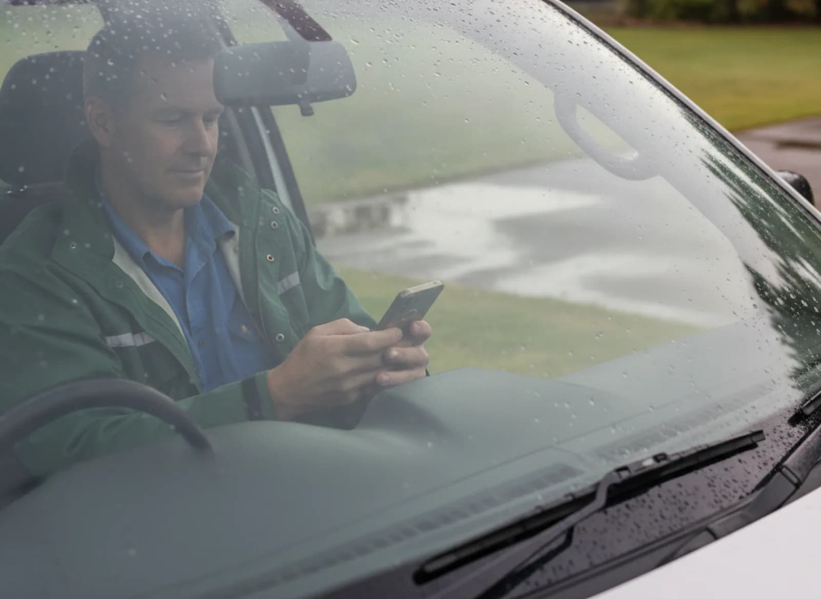 A gardener reading his phone in his ute on a wet morning